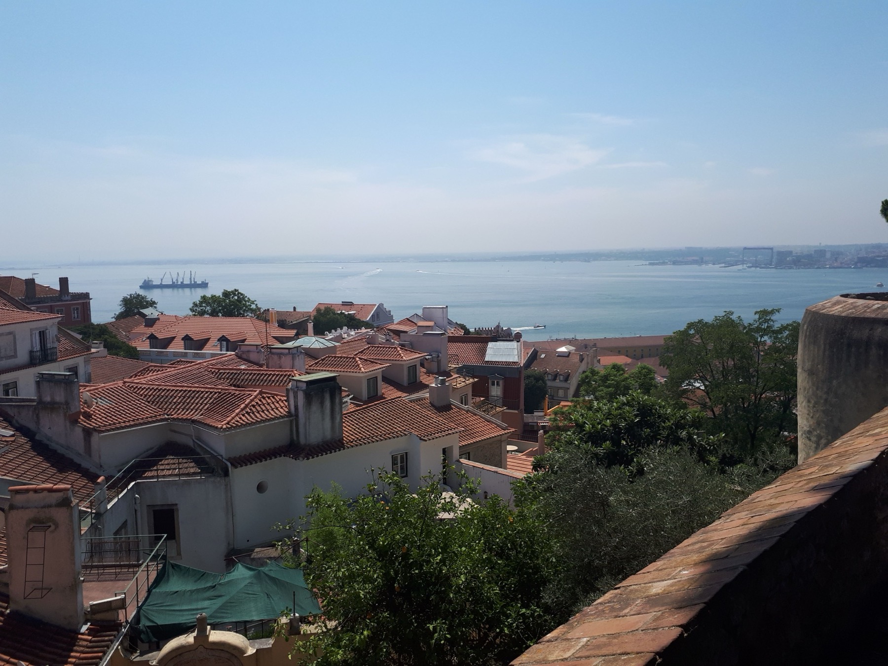 Rooftop view over a sea of orange terracotta-tiled Lisbon rooftops down to the Tagus river under a clear blue sky