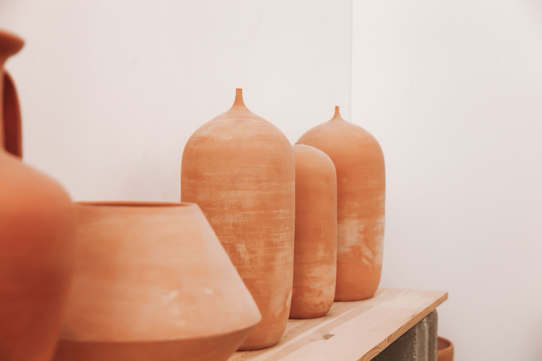 A row of handmade terracotta clay vessels in warm earth tones against a limewashed white wall