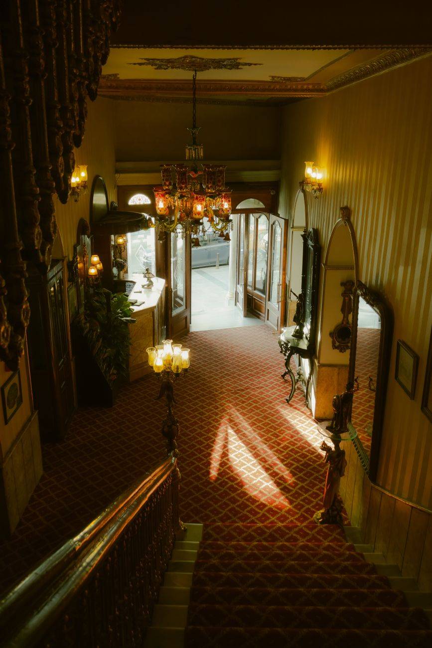 Sunlit, vintage hotel lobby in İstanbul with a grand staircase and ornate chandeliers.