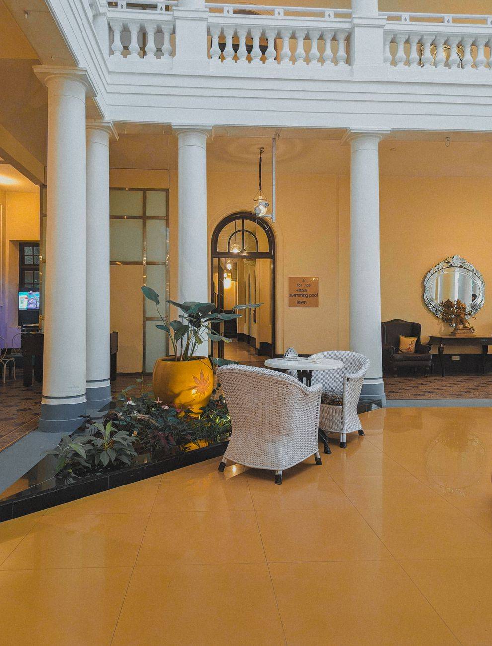 Luxurious hotel lobby with wicker armchairs, ornate columns, and lush plants in Krishnarajasagara, India.