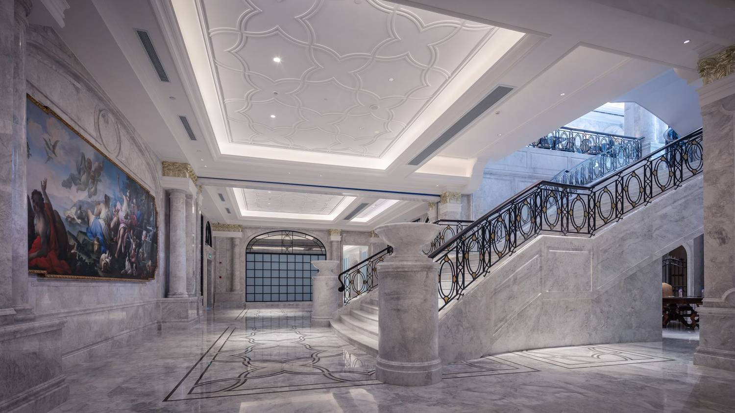 Elegant marble hallway featuring a grand staircase and ornate ceiling design.