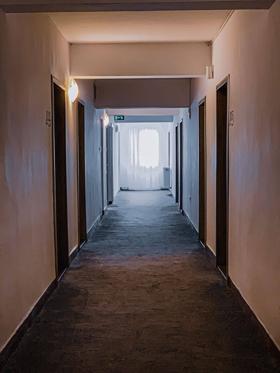 Perspective view of empty corridor of apartment building with doors and lamps on white walls and window in modern house