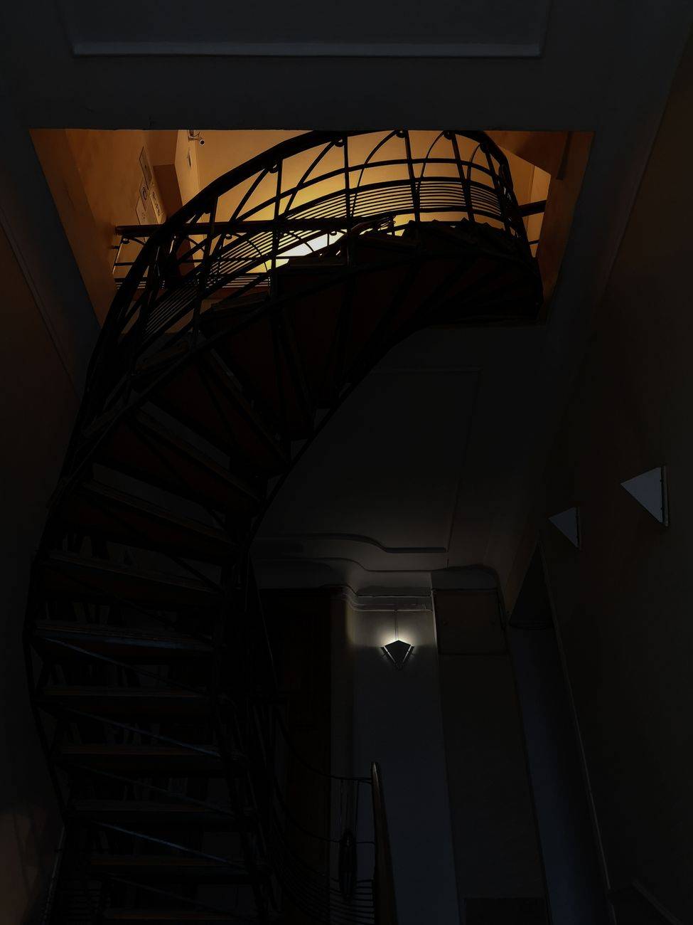A dramatic view of a spiral staircase with intricate shadows and light play in an indoor setting.