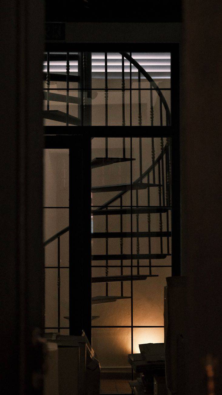 A moody silhouette of a spiral staircase illuminated by soft lighting, indoors.