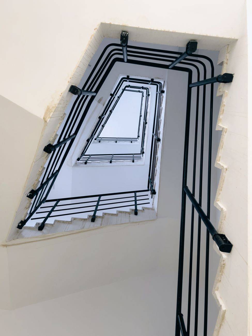 Geometric perspective of a modern spiral staircase with black handrails in a white interior.