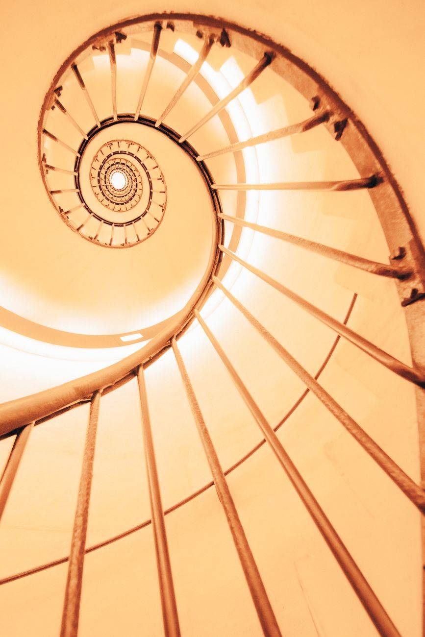 Upward view of a modern spiral staircase with an abstract geometric pattern and warm lighting.
