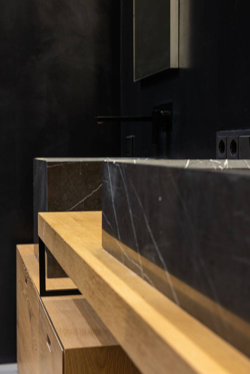 Part of marble washbasin with faucet placed on wooden cabinet in light stylish washroom with black wall and mirror at home