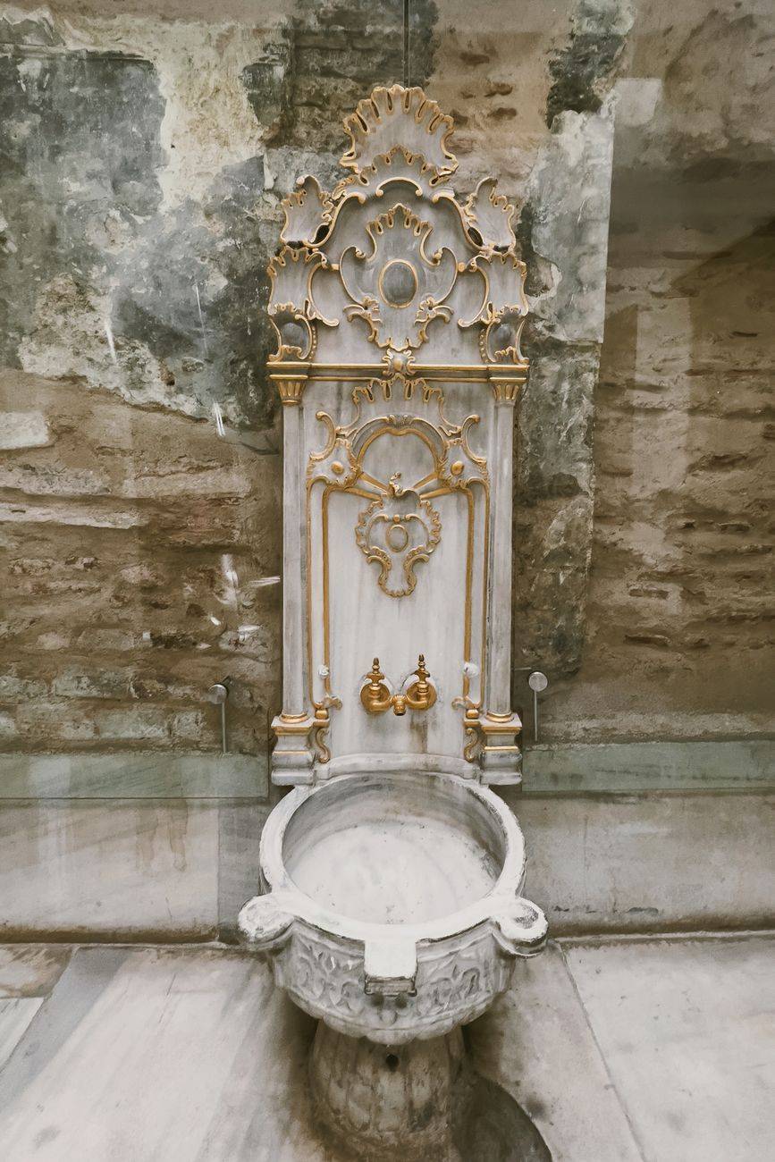 Elegant marble fountain with gold accents against a rustic wall. Perfect for decor and architectural themes.