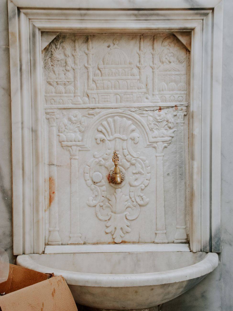 Close-up of an ornate marble fountain featuring detailed carvings and a brass faucet in a classic architectural style.