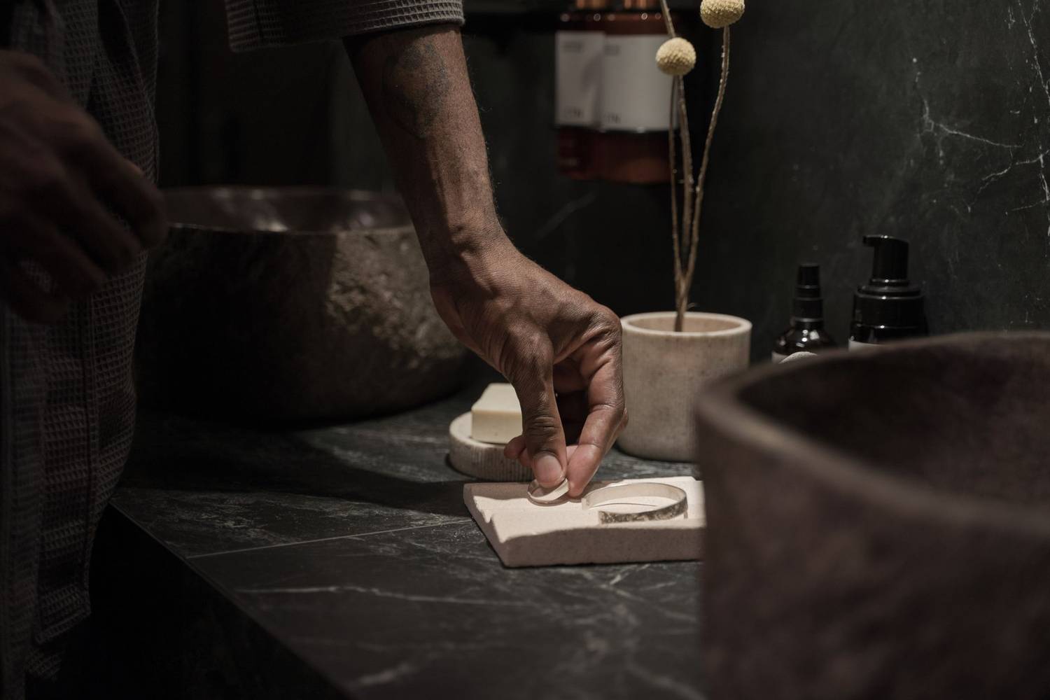 A hand reaches for a handmade silver bracelet in a modern bathroom with a minimalist style.