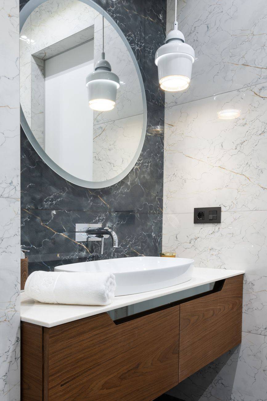 Interior of light bathroom with round mirror and white sink on cabinet near lamp