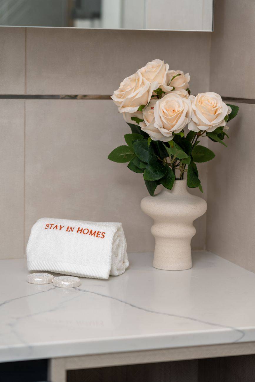 A stylish bathroom counter with a white vase of roses and a personalized towel.