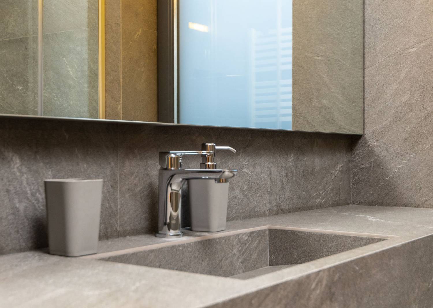 Chrome faucet and marble sink under mirror in modern bathroom with tiled walls