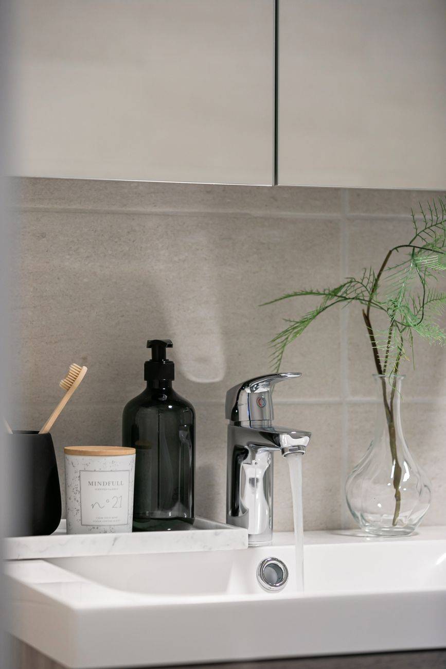 A stylish bathroom sink with running water, a glass vase, bottle, cup, and toothbrush for a modern design.