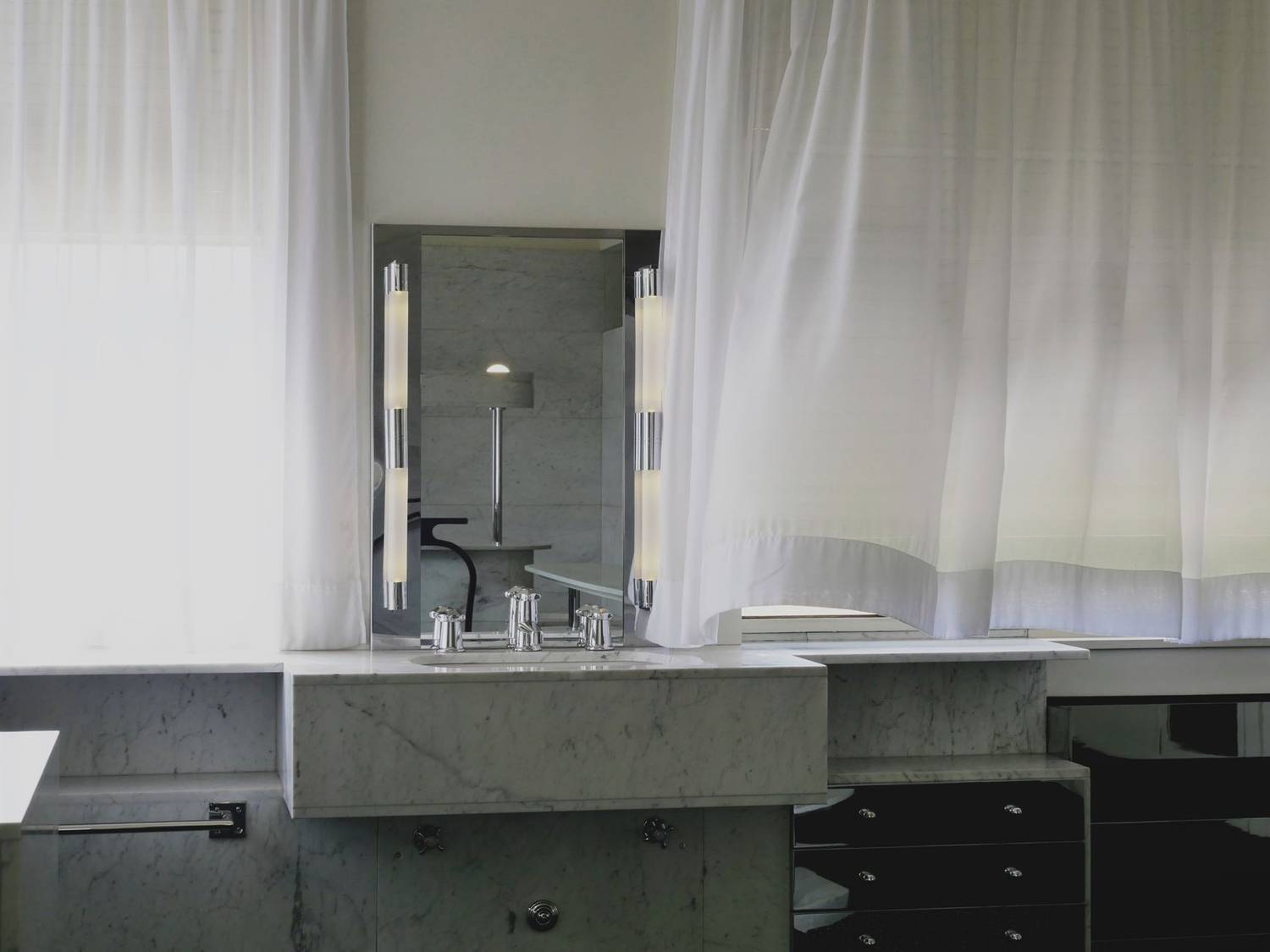 A modern bathroom interior featuring a marble sink, mirror, and sheer curtains for a stylish look.