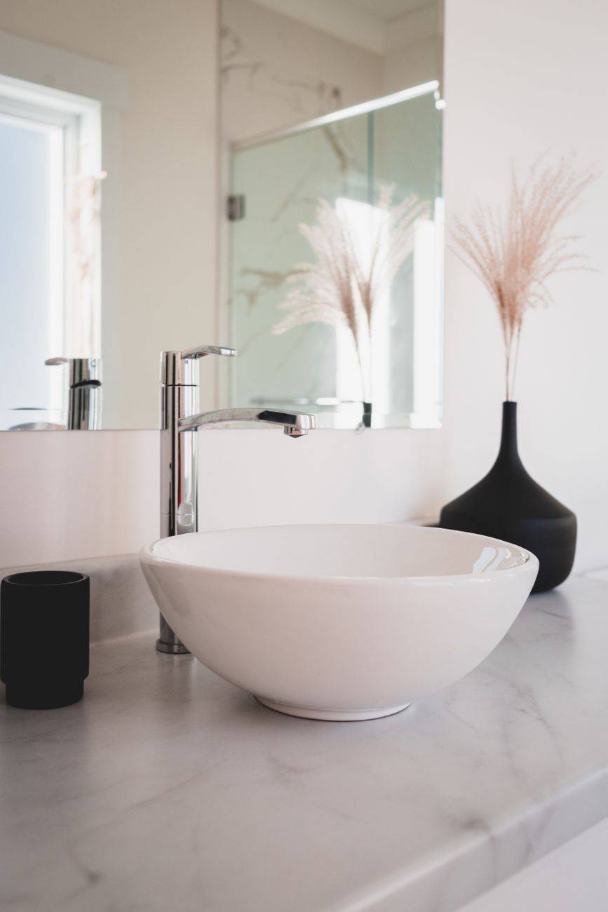 Interior of modern bathroom with white ceramic washbasin near decorative ears in vase and mirror on wall