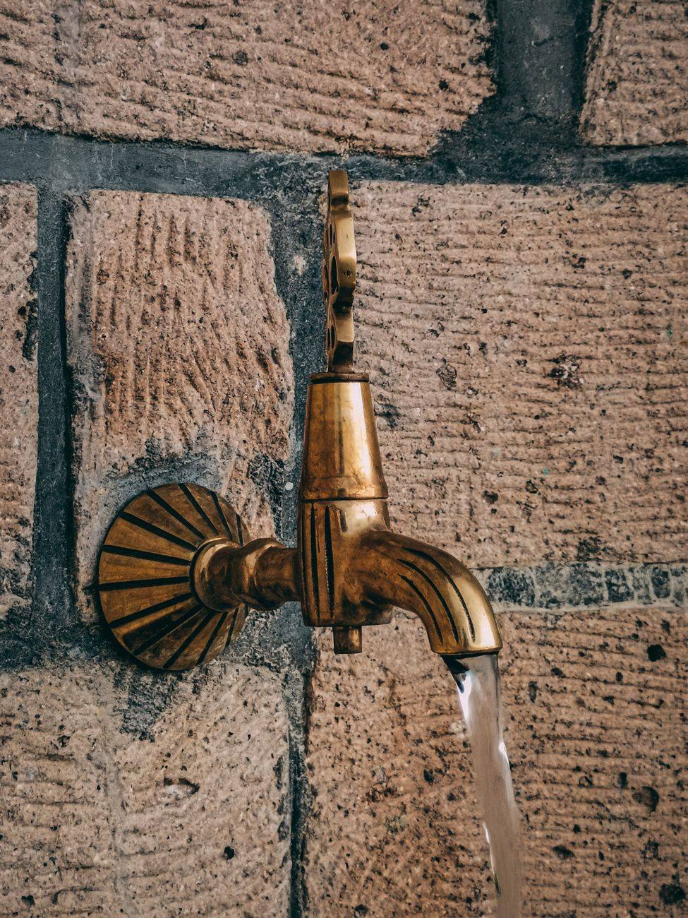 Close-up of a vintage brass faucet mounted on a textured stone wall with water flowing.