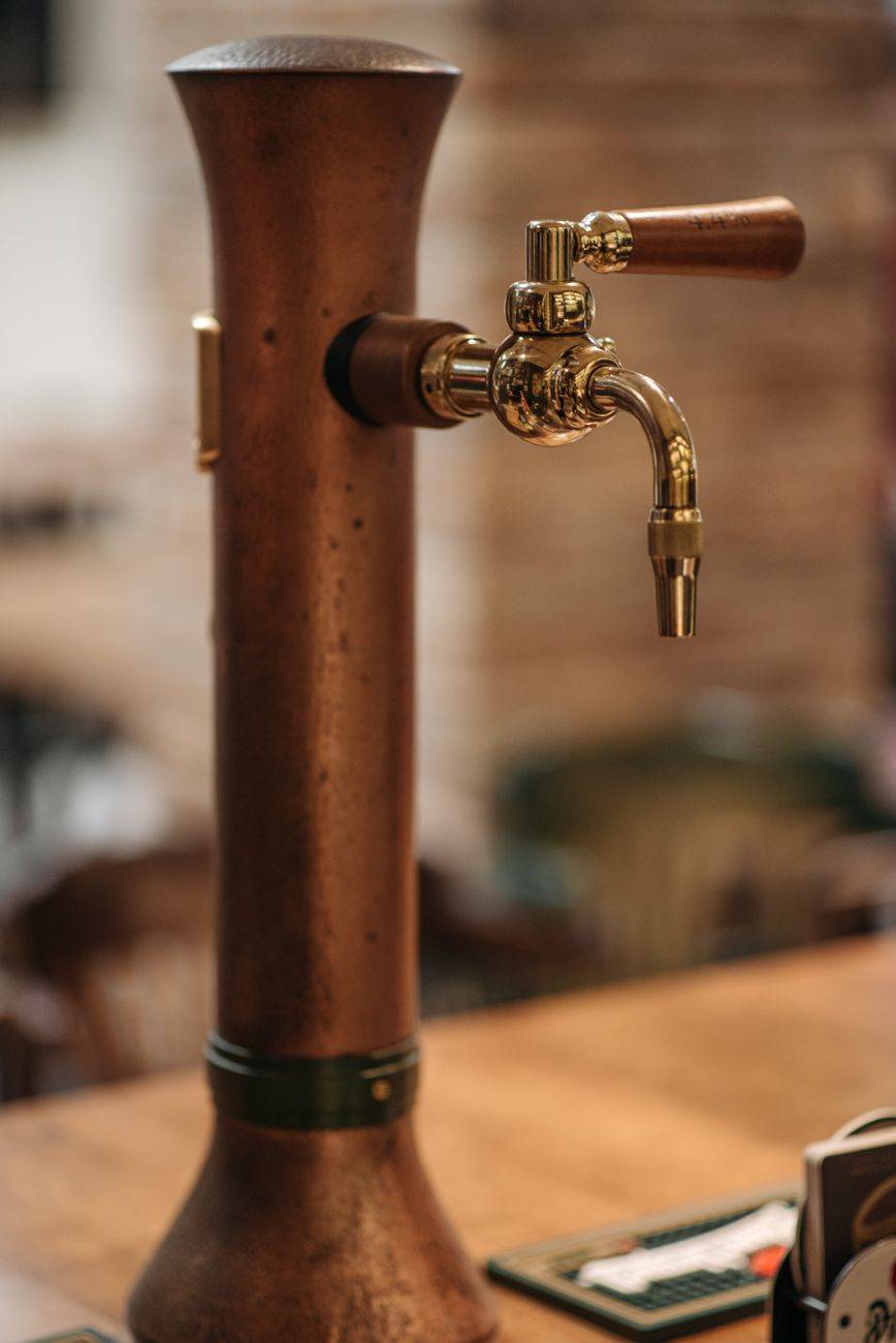 A vintage copper beer tap with a wooden handle in an inviting indoor bar setting.