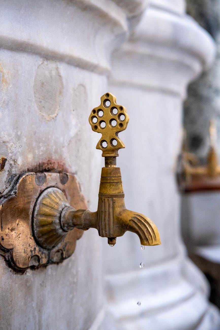 Close-up of an ornate brass tap with a decorative design on a marble fountain.