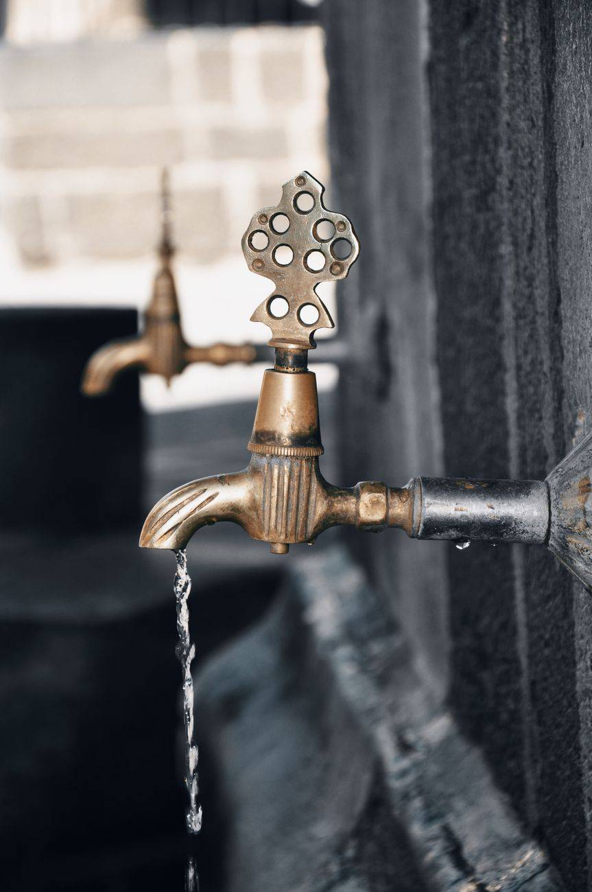 Detailed close-up of a vintage brass faucet with water flowing, showcasing intricate design.