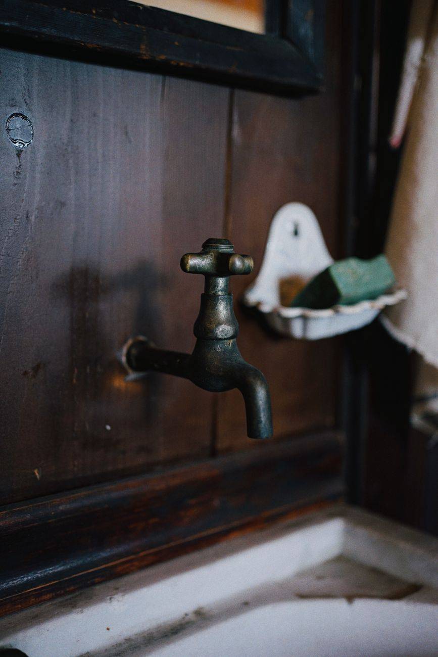 A close-up of a vintage brass faucet against a wooden wall with a rustic sink.