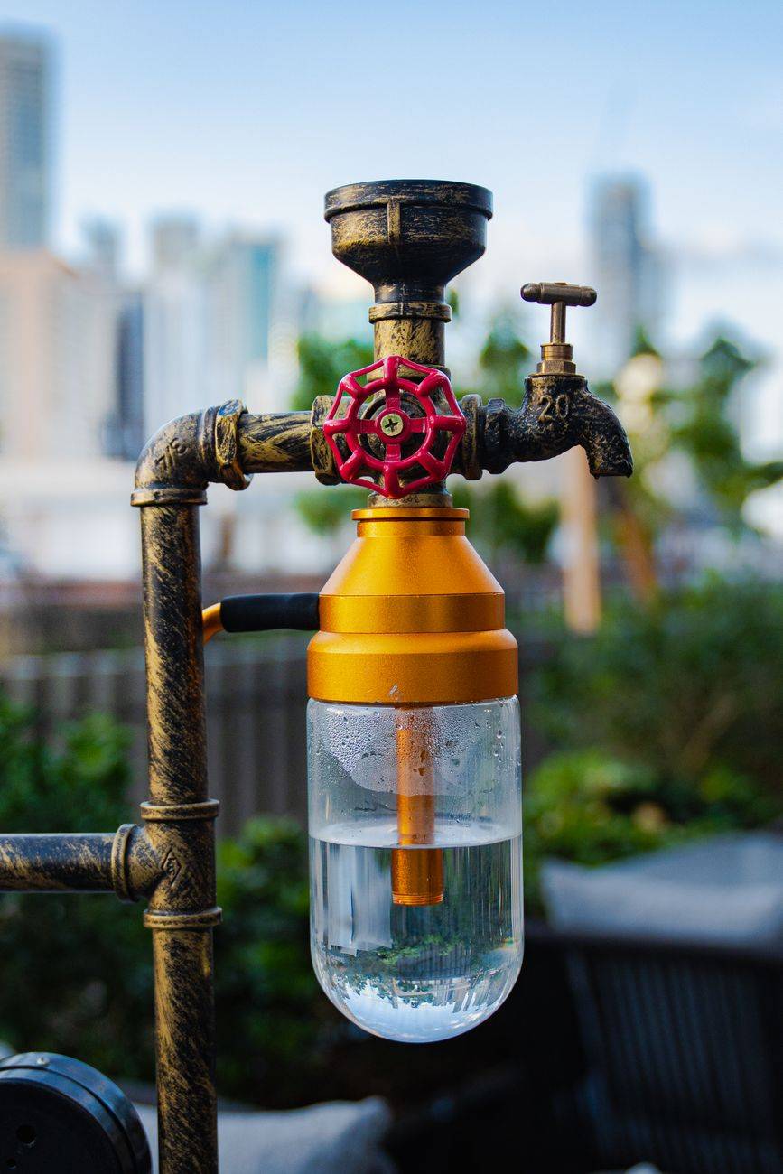 Vintage water pipe with modern filter in urban setting, Dubai skyline in background.