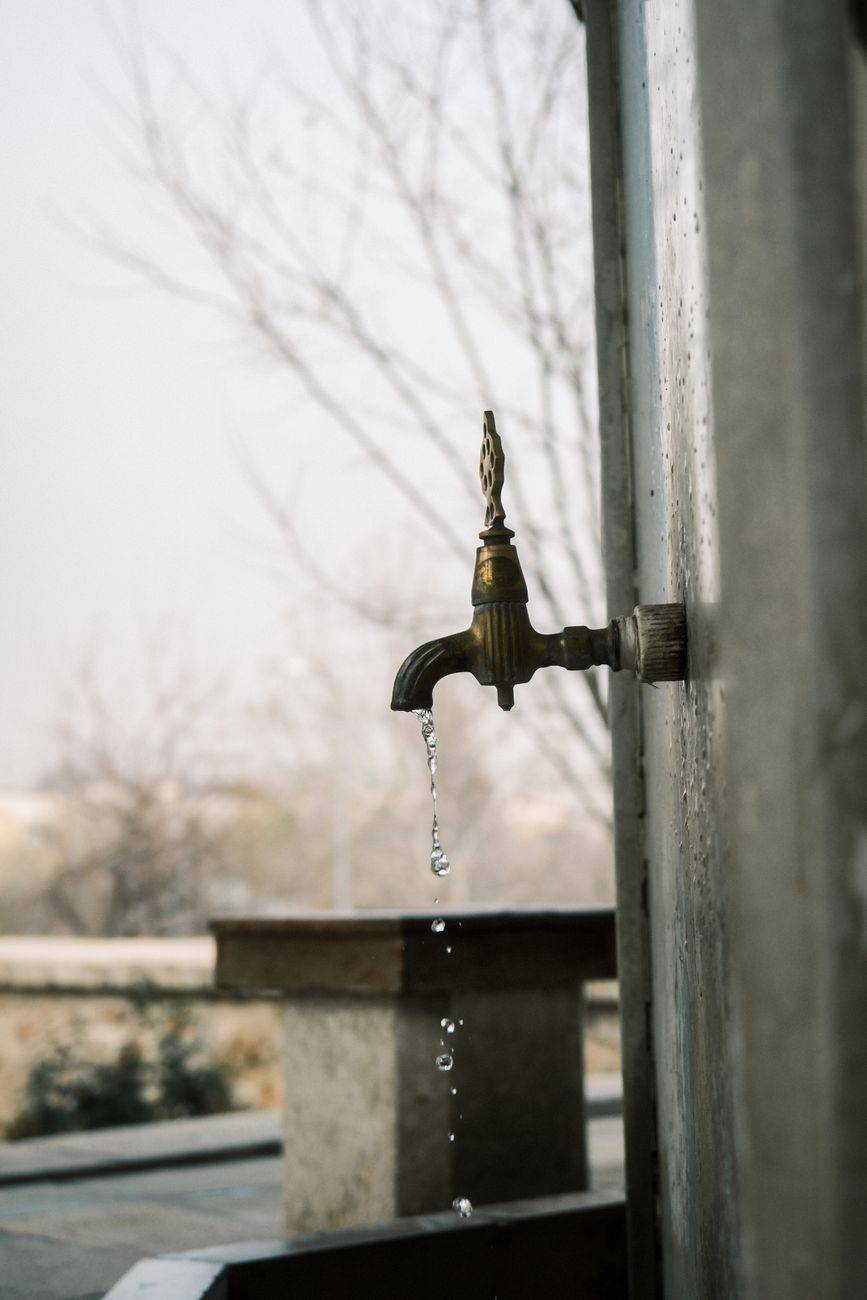 Close-up of a vintage water faucet outdoors dripping water droplets.