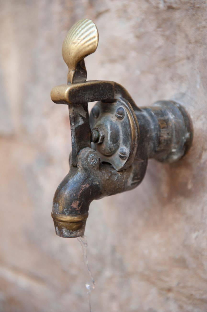 Close-up of an antique brass faucet dripping water on a textured wall background.