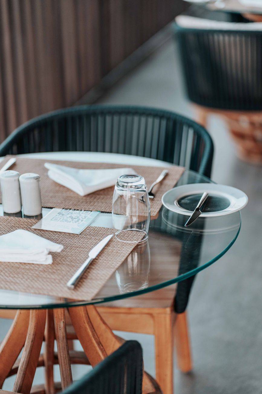 Glass-top table with cutlery and napkins at an elegant restaurant setting. Ideal stock for hospitality themes.