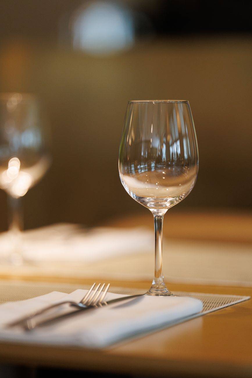 An elegant fine dining table setting featuring a clear wine glass and cutlery on a napkin.