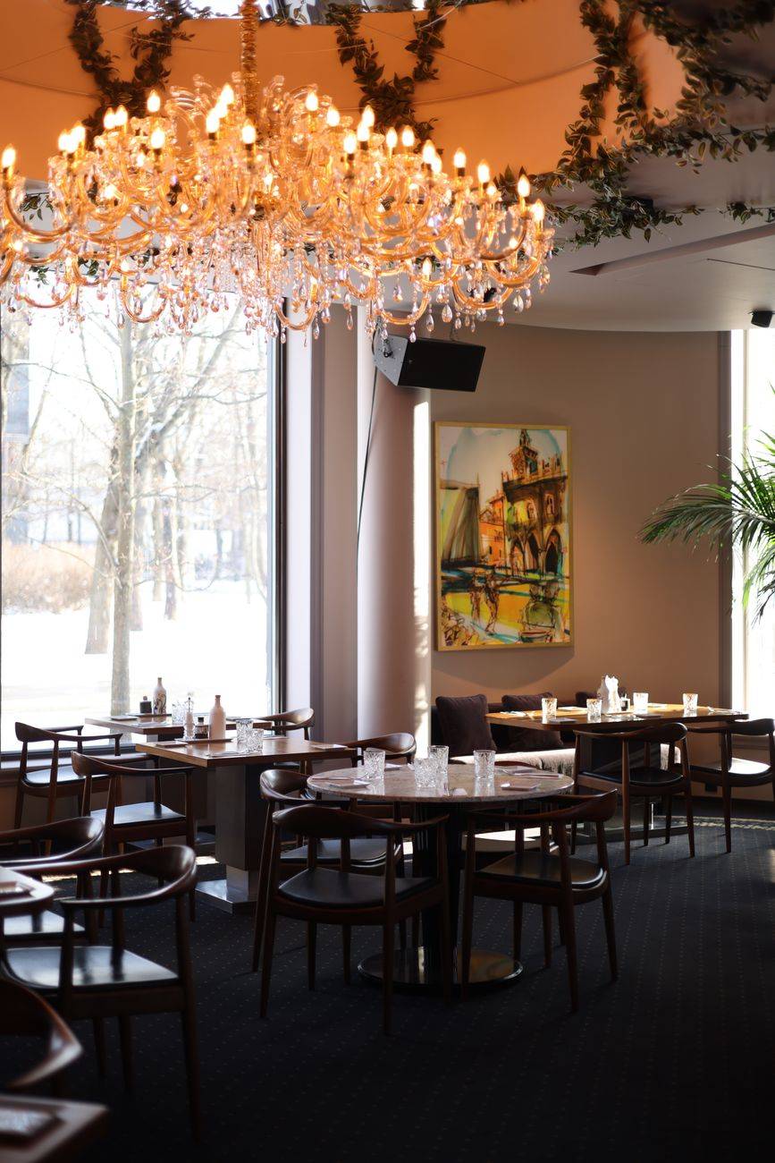 Luxurious restaurant interior featuring a crystal chandelier and stylish dining setup, captured in daylight.