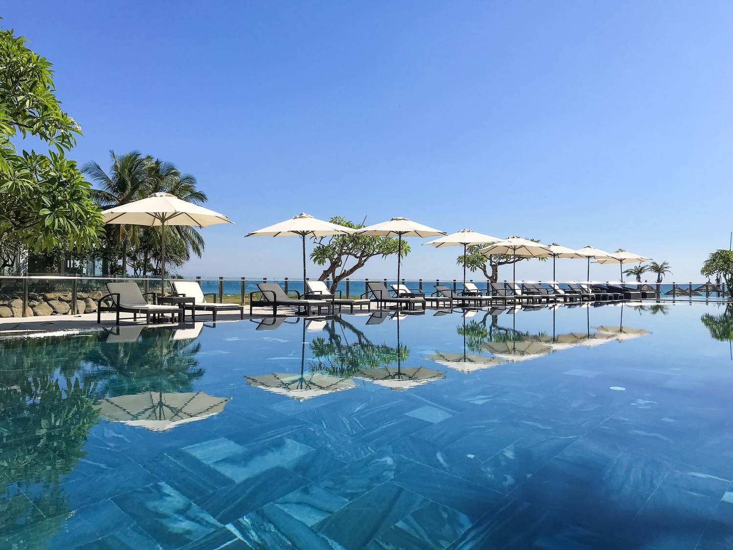 Stunning poolside view with loungers and umbrellas by the ocean, perfect for a tropical vacation.