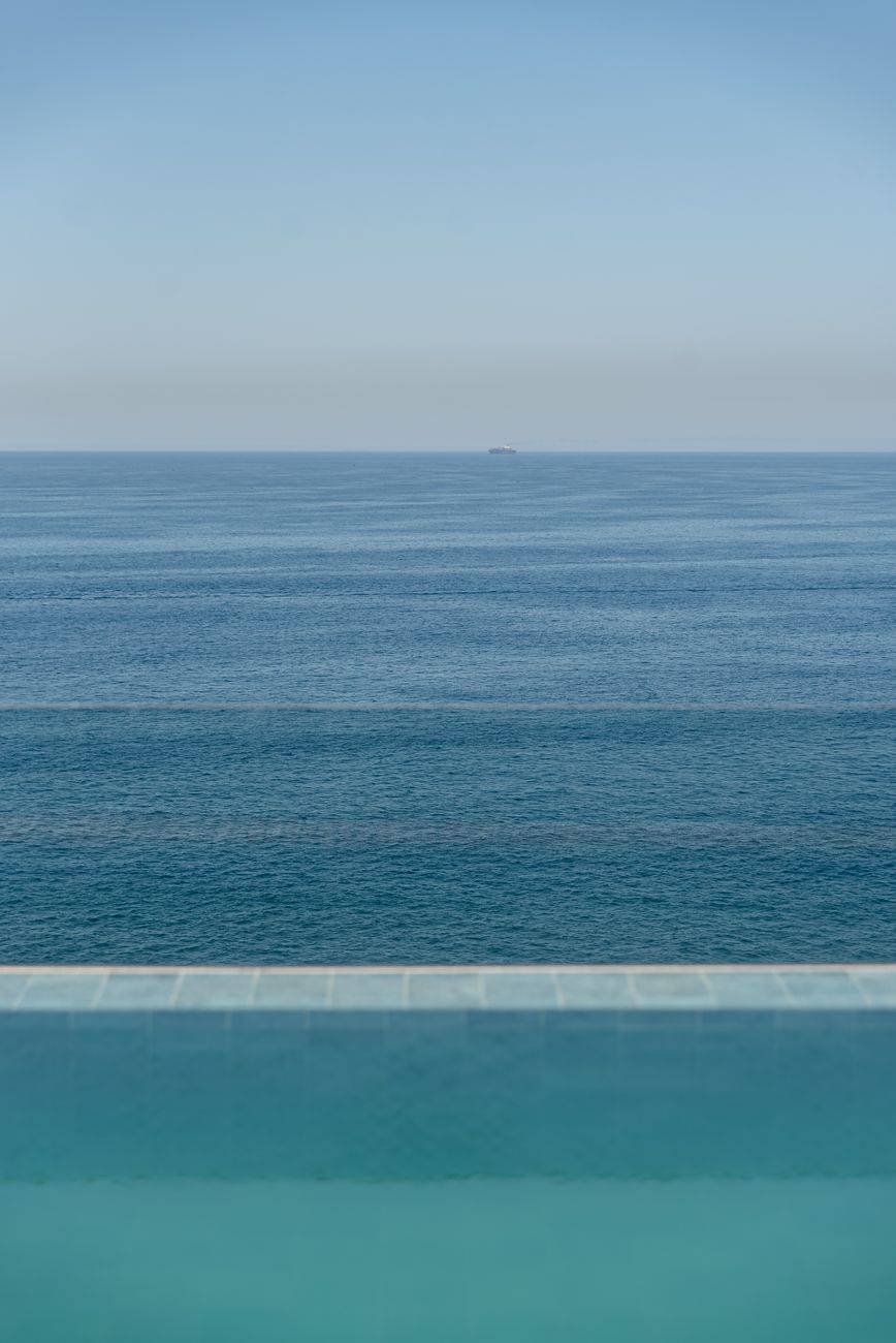 A tranquil view of an infinity pool seamlessly blending into the ocean horizon under a clear blue sky.