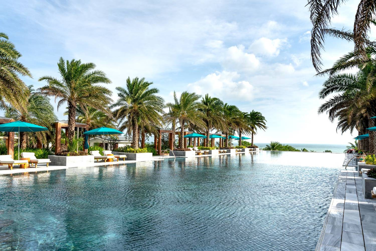 Relaxing scene of a luxury resort pool lined with palm trees and ocean view under a clear sky.