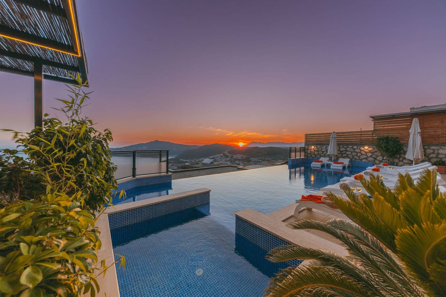 Infinity pool at a luxury resort with a stunning sunset view, lush plants, and clear skies.