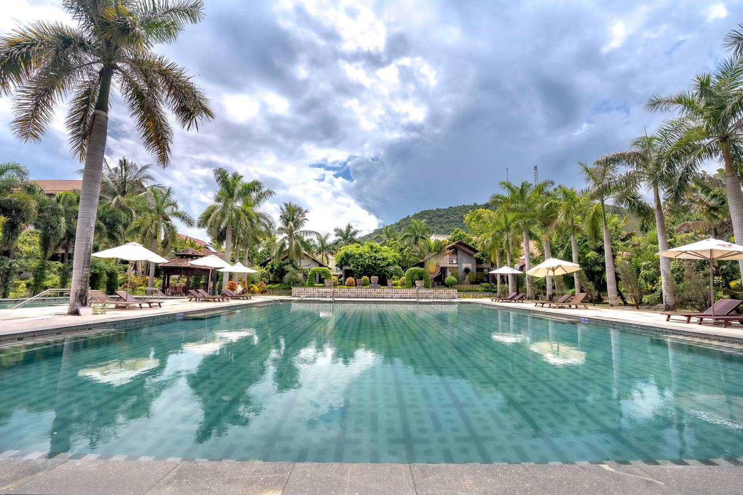 A tranquil tropical resort featuring a stunning pool surrounded by palm trees under a dramatic sky.