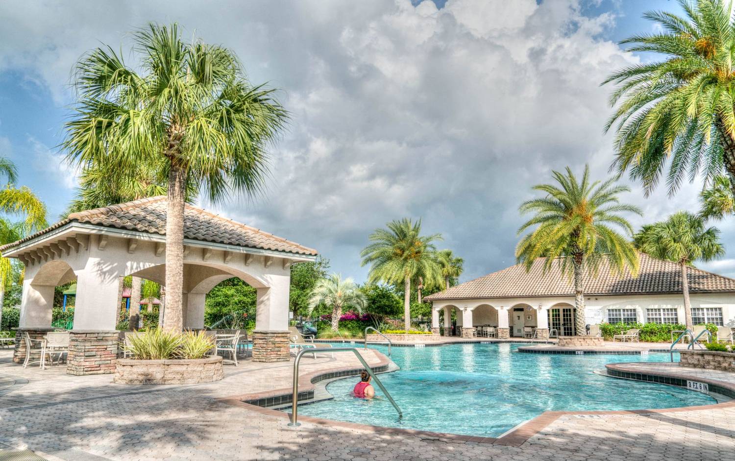 Beautiful tropical resort poolside scene featuring palm trees and inviting water under a cloudy sky.