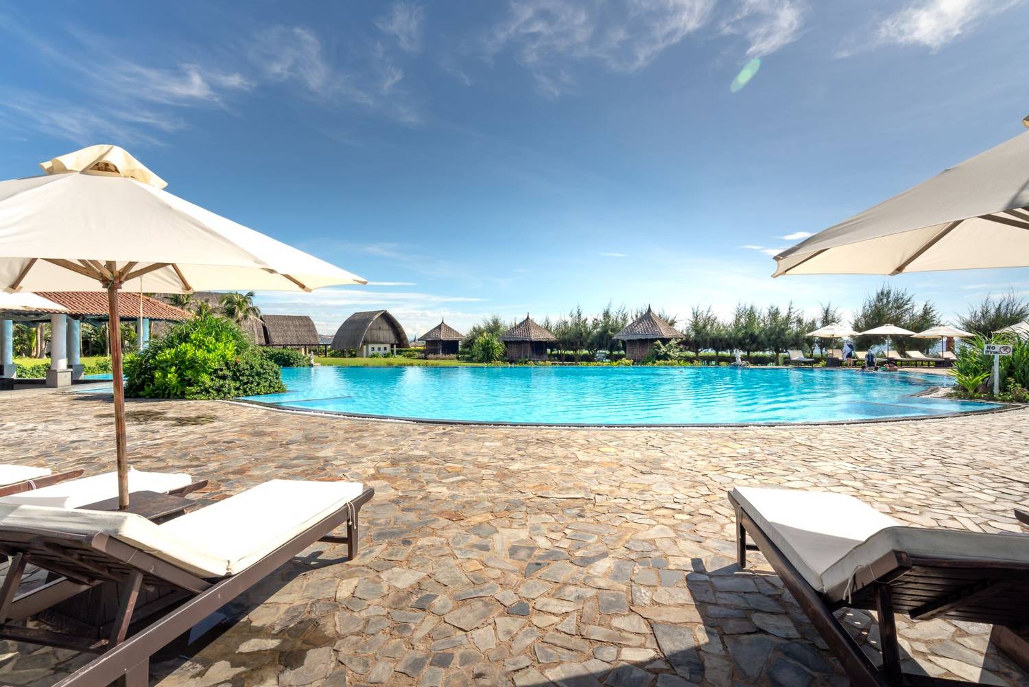 Serene poolside view with lounge chairs and umbrellas at a tropical resort, ideal for relaxation.