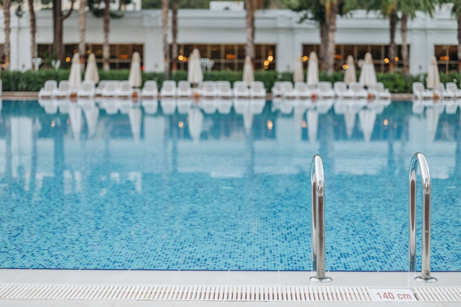 Bright and tranquil view of a resort swimming pool with ladder and deck chairs.