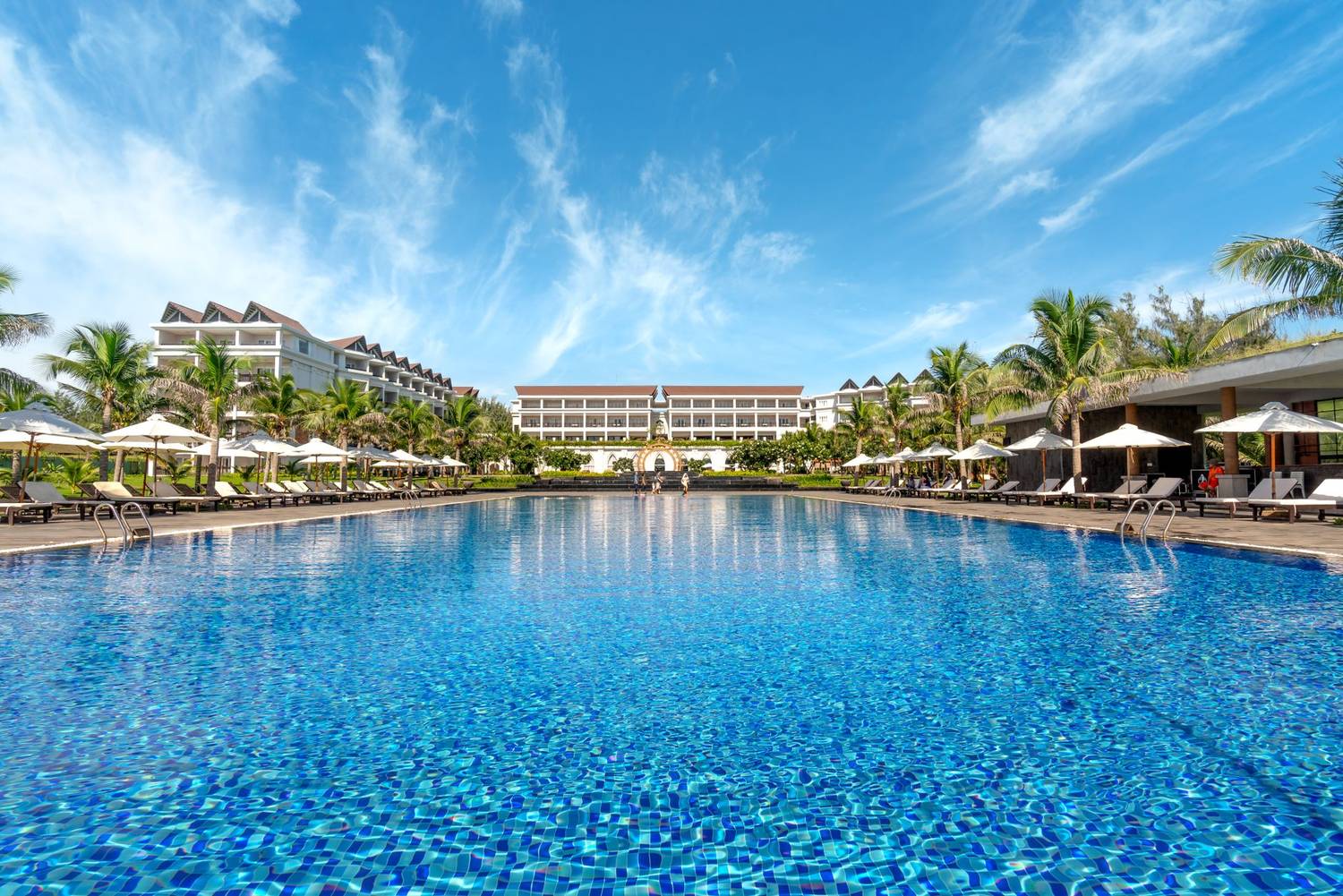Beautiful resort pool framed by deck chairs and palm trees under a vibrant sky, perfect for a summer getaway.