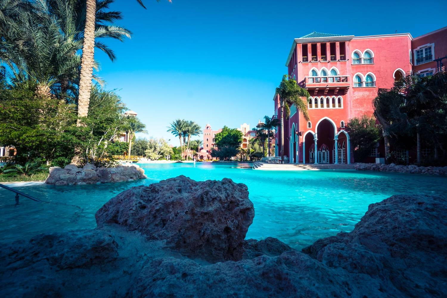 Stunning resort poolside area with palm trees and vibrant red architecture on a sunny day.