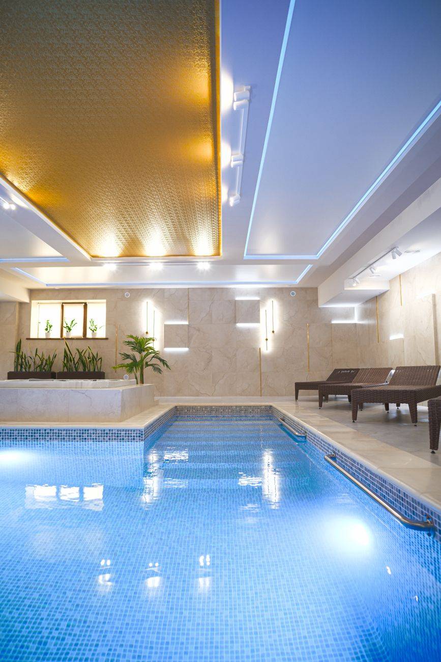 Elegant indoor pool area featuring modern lighting and stylish sunbeds.