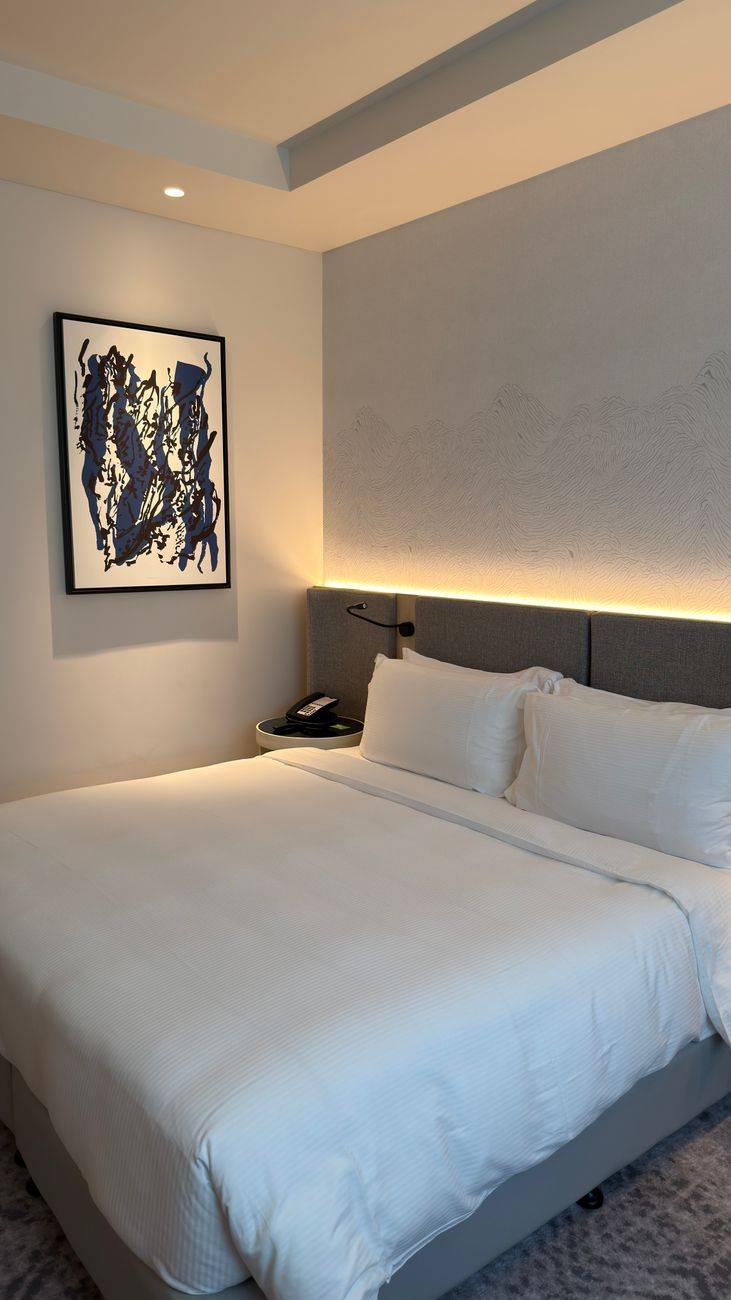 Elegant hotel room with modern decor, cozy bedding, and abstract art on the wall.