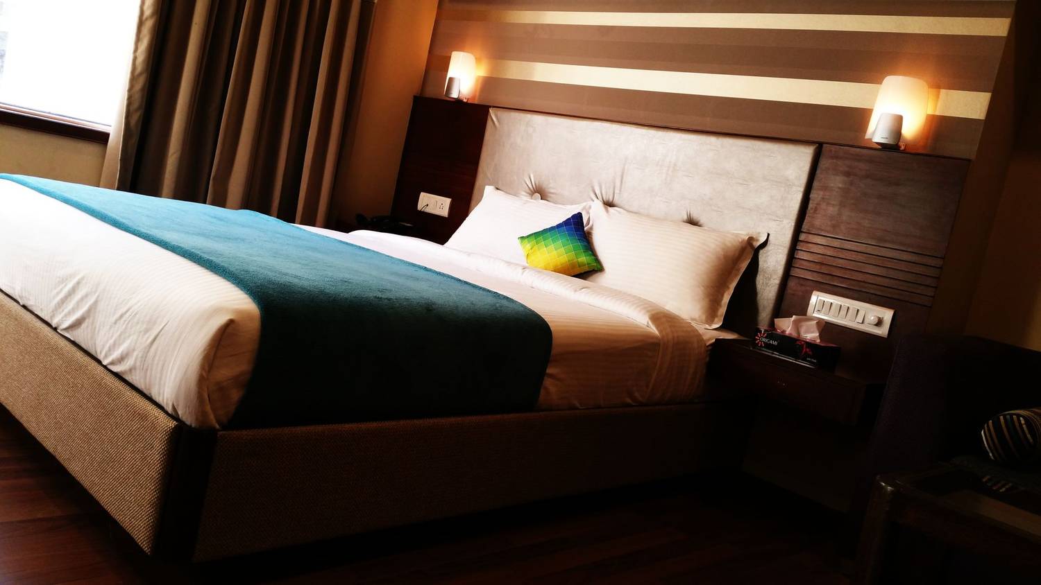 A contemporary hotel room featuring a large bed with colorful pillows, warm lighting, and modern interior design.