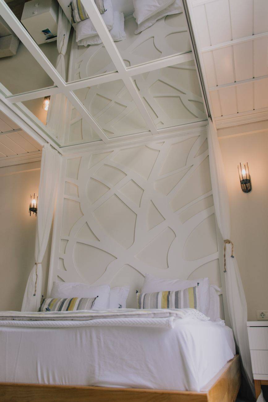 Elegant hotel room interior with white bed, stylish headboard, and mirrored ceiling.
