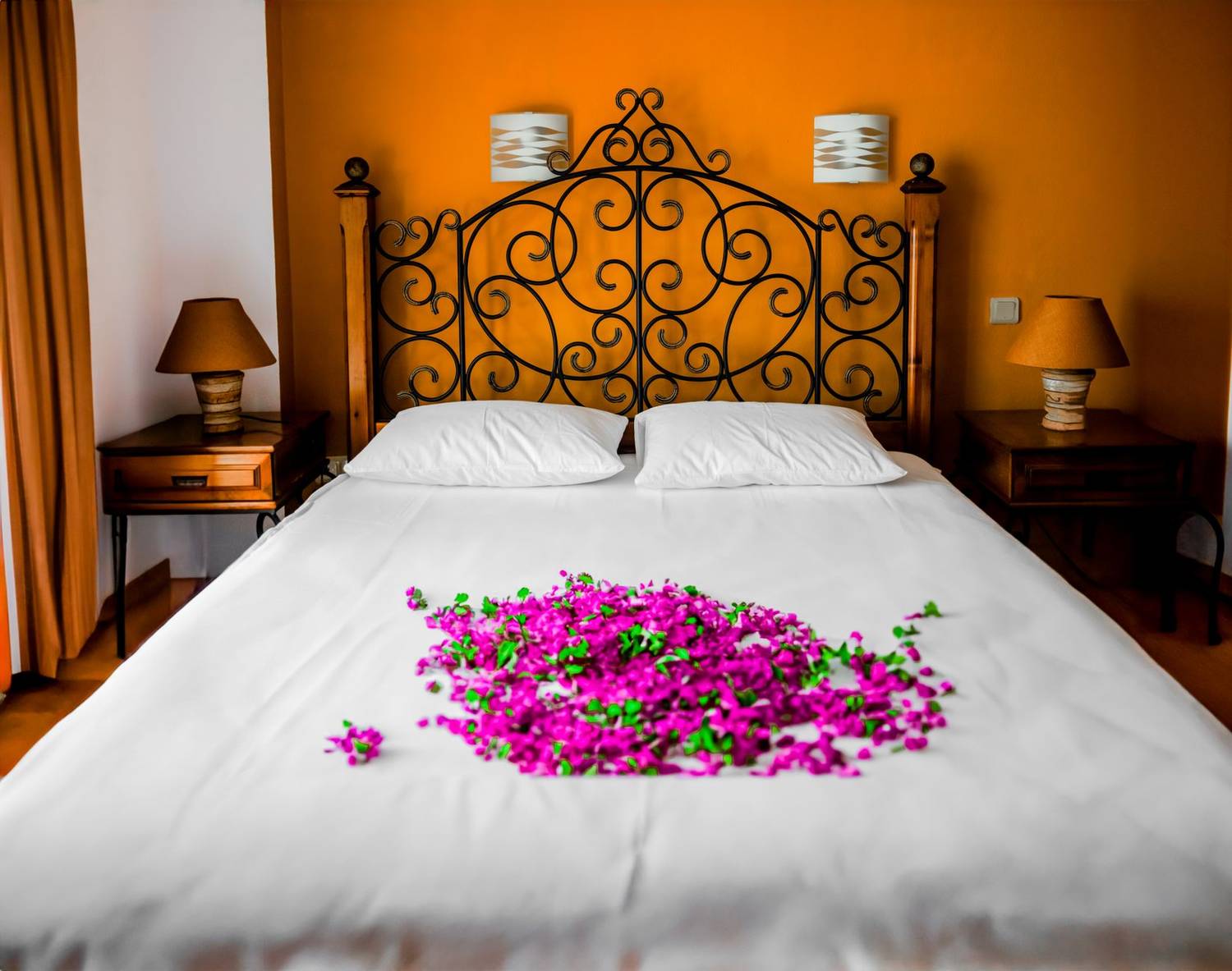 Elegant bedroom with iron headboard and purple petals on white bedding, ideal for romantic getaways.