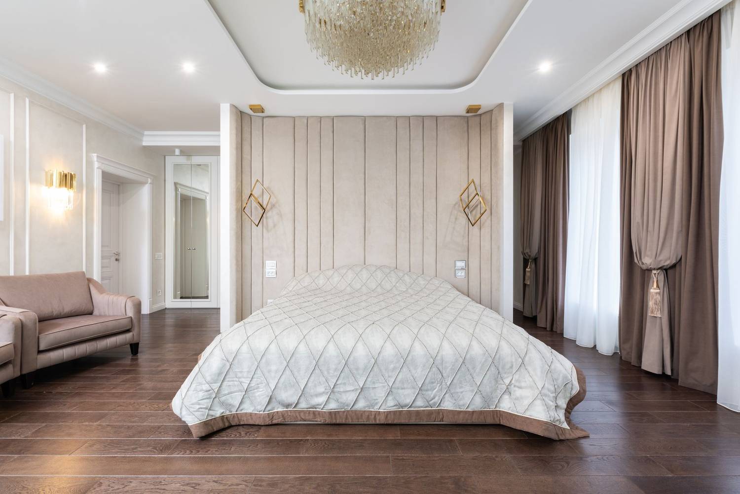 Interior of modern bedroom with bed next to armchairs under chandelier with curtains on windows
