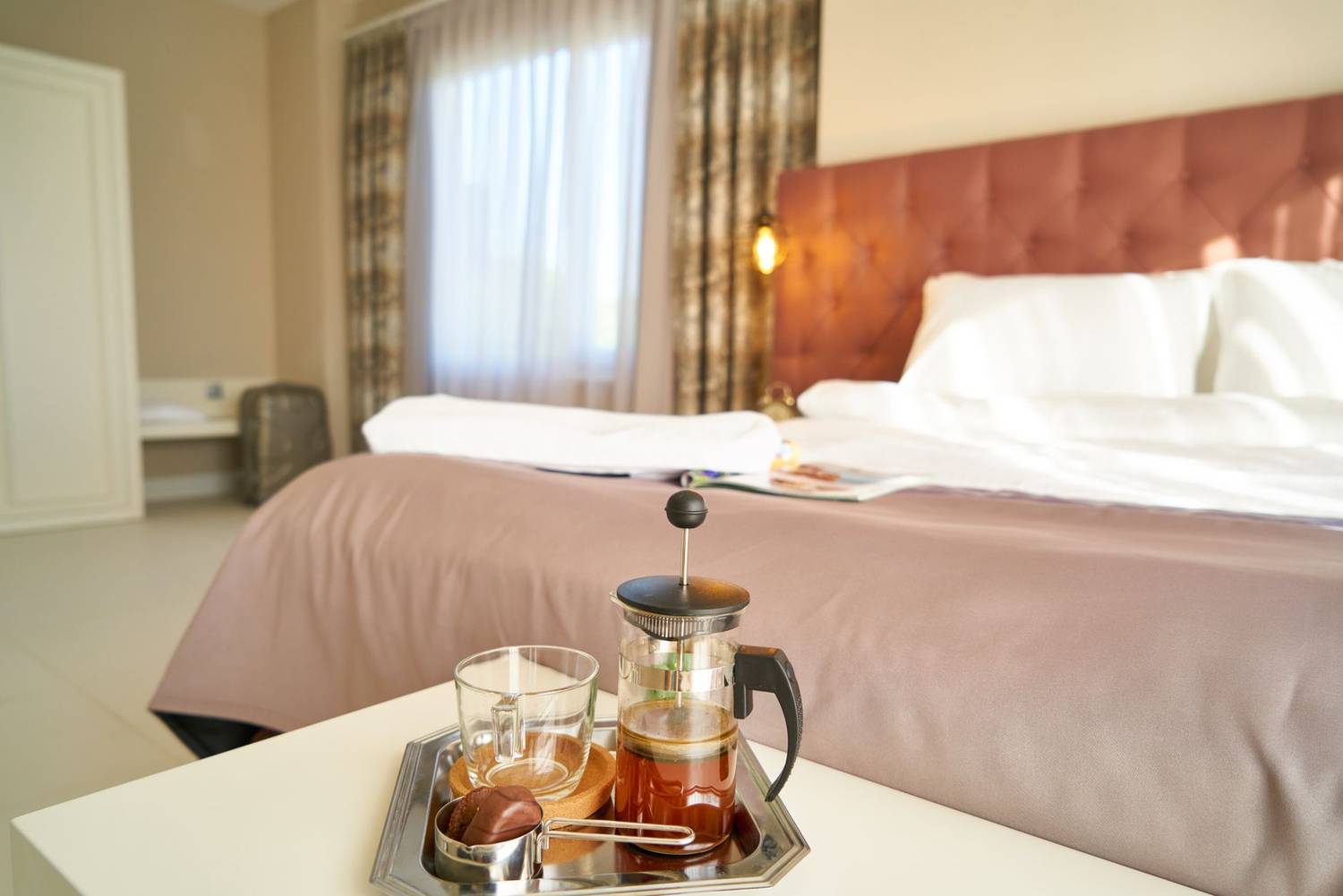 Inviting hotel room with a French press coffee setup on the bedside table, perfect for relaxation and travel.