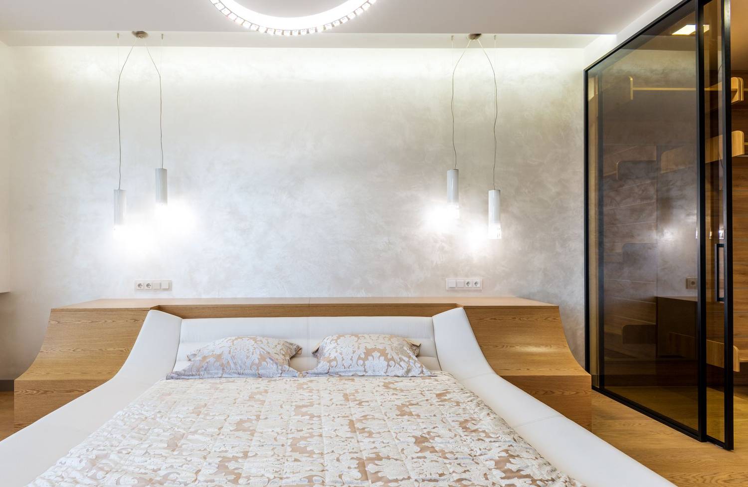 Stylish interior design of spacious bedroom lighted with set of lamps furnished with bed and wardrobe closet with glass doors