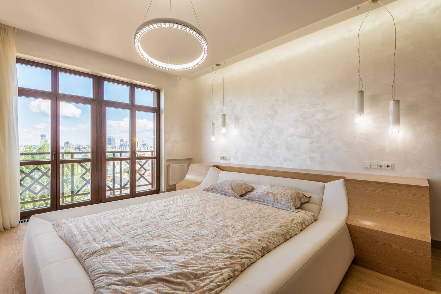 Modern new interior design of bedroom furnished with comfortable bed and lighted with ceiling chandelier and bedside lamps against window an